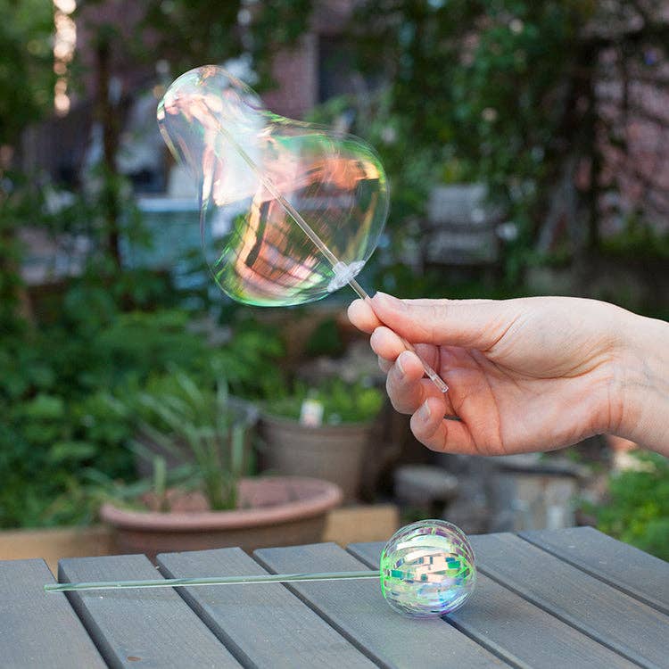 Hand holding an iridescent twirler wand  in motion, set against a garden background