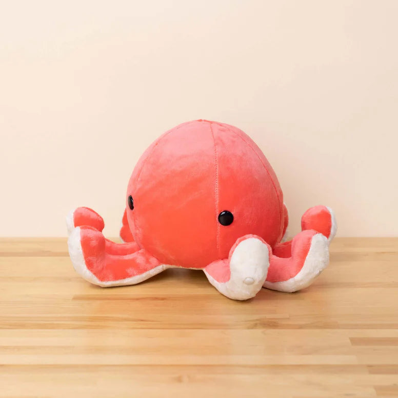 Red and white plush octopus toy on a wooden surface with a beige background. It has upturned tentacles and round black eyes.