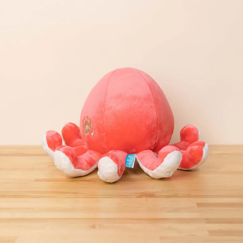 Red and white plush octopus toy on a wooden surface with a beige background. It has upturned tentacles and round black eyes.