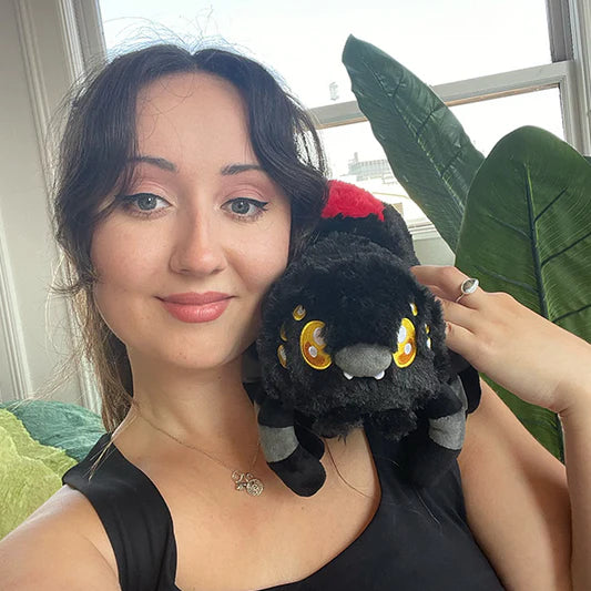 Woman holding a black and red plush toy resembling a black widow spider with yellow cartoon eyes indoors