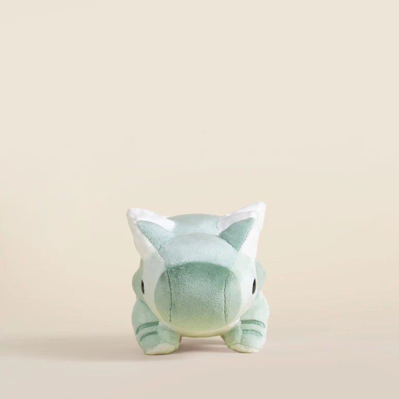 Plush toy ankylosaurus dinosaur with a light green body and white accents on a beige background