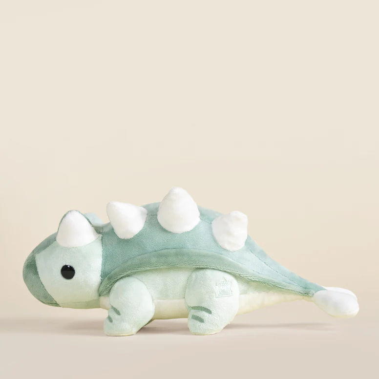 Plush toy ankylosaurus dinosaur with a light green body and white accents on a beige background