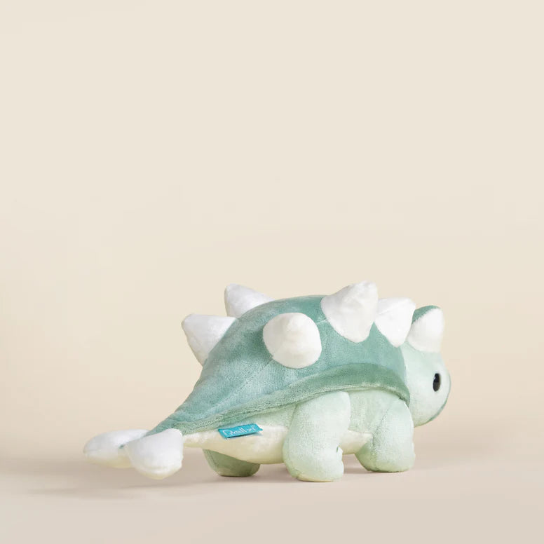 Plush toy ankylosaurus dinosaur with a light green body and white accents on a beige background