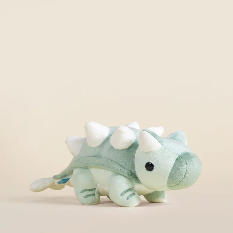 Plush toy ankylosaurus dinosaur with a light green body and white accents on a beige background