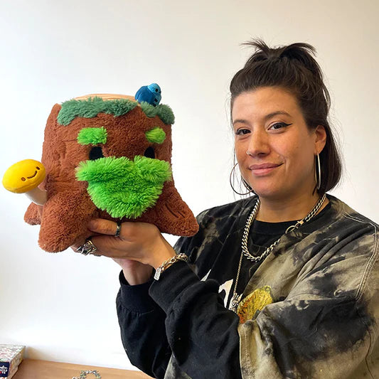 Person holding a plush toy resembling a tree stump with a smiling expression