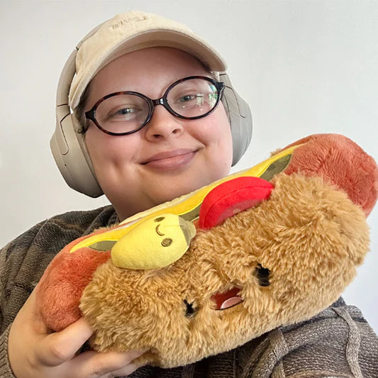 Person wearing headphones holding a plush toy resembling a hot dog with a face.