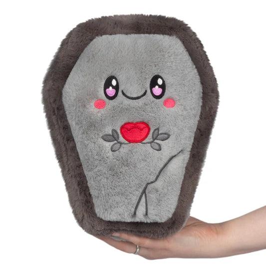 Plush toy resembling a coffin with a face and red flower on a white background