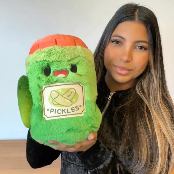 Person holding a green plush toy with a red lid labeled 'Pickles'.